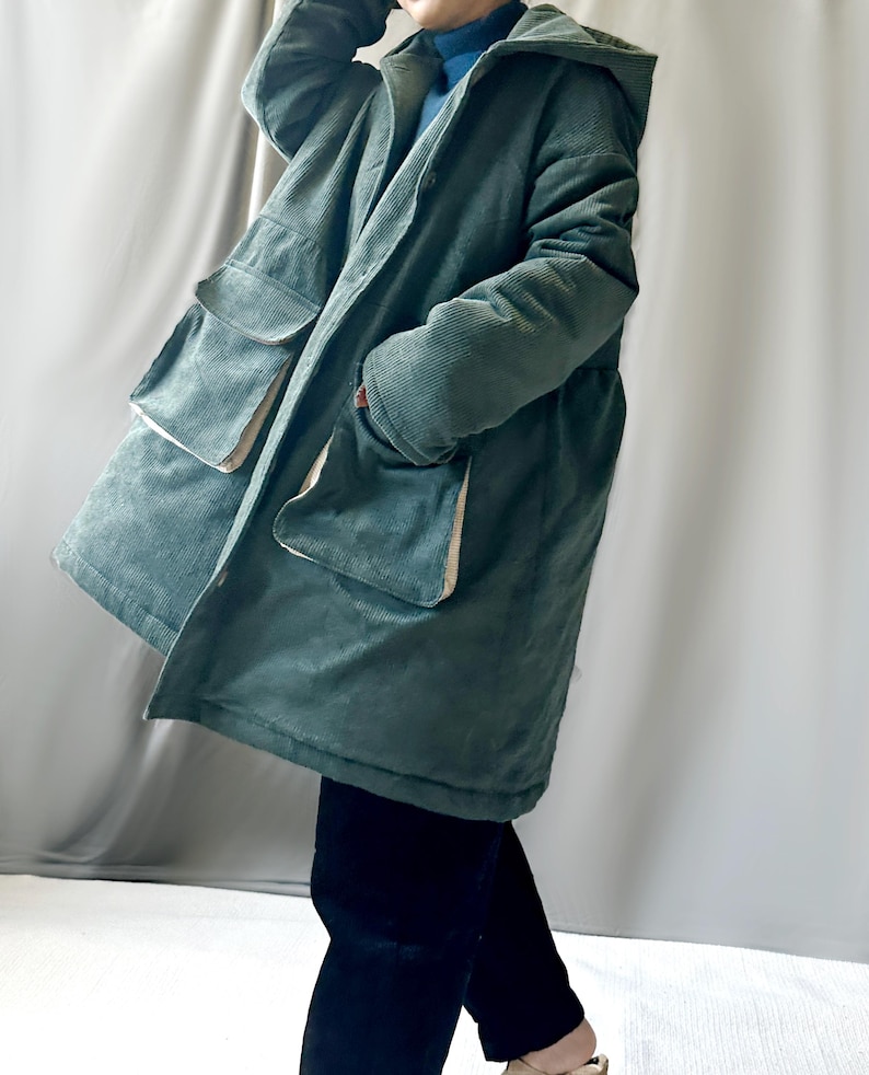 May include: A long, green corduroy jacket with a hood and large pockets. The jacket has a zipper closure and a button closure.