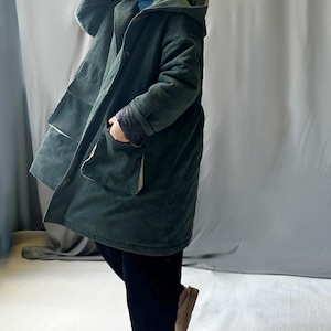 May include: A long, dark green corduroy coat with a hood and large pockets. The coat is lined with a lighter fabric and has a button closure.
