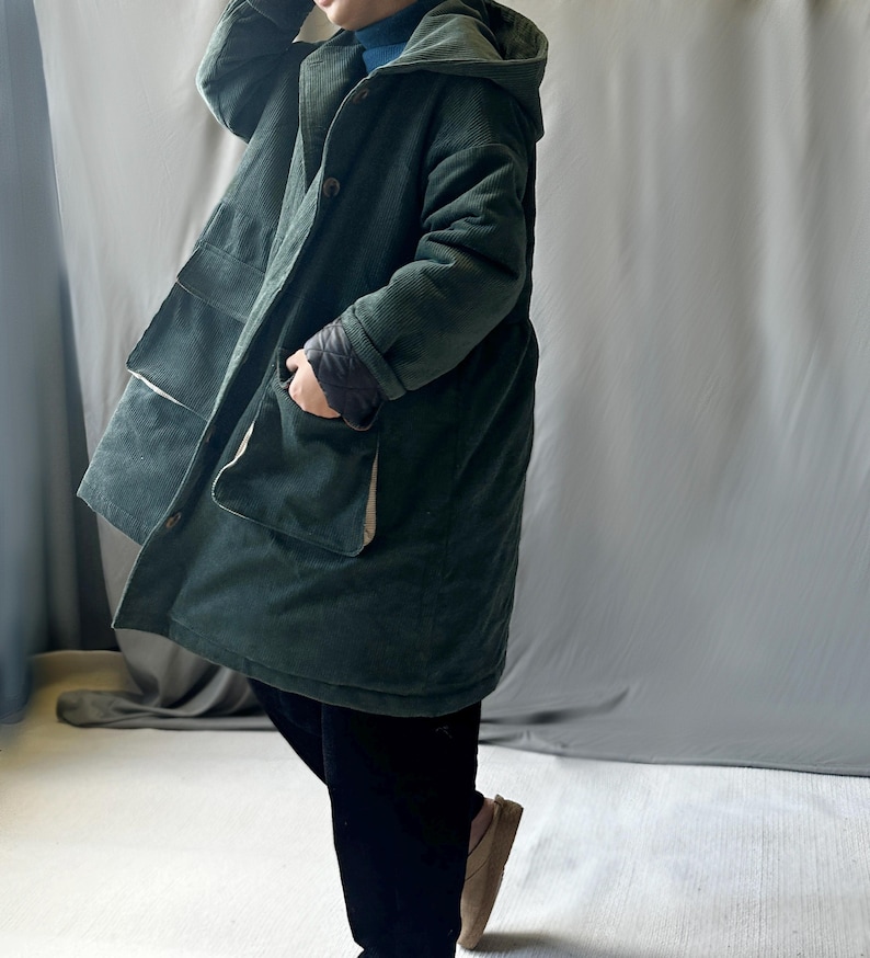 May include: A long, dark green corduroy coat with a hood and large pockets. The coat is lined with a lighter fabric and has a button closure.