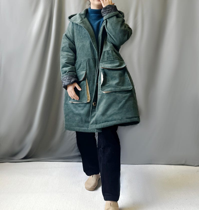 May include: A long, green corduroy coat with a hood and large pockets. The coat has a button closure and a quilted lining.