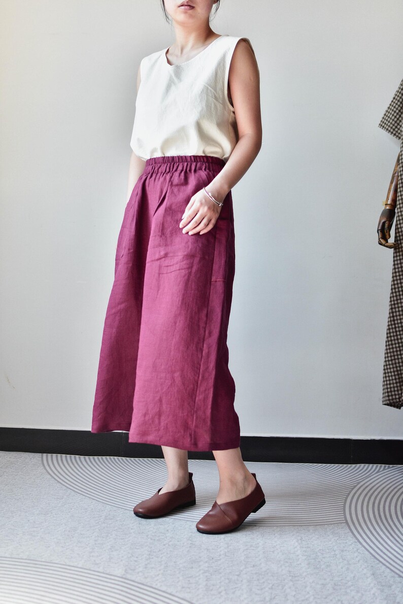 Puede incluir: Una camiseta sin mangas de color crema combinada con una falda burdeos de pernera ancha. La falda tiene cintura alta y bolsillos. Zapatos de cuero marr&oacute;n completan el conjunto. El conjunto es sencillo y elegante, adecuado para uso informal.