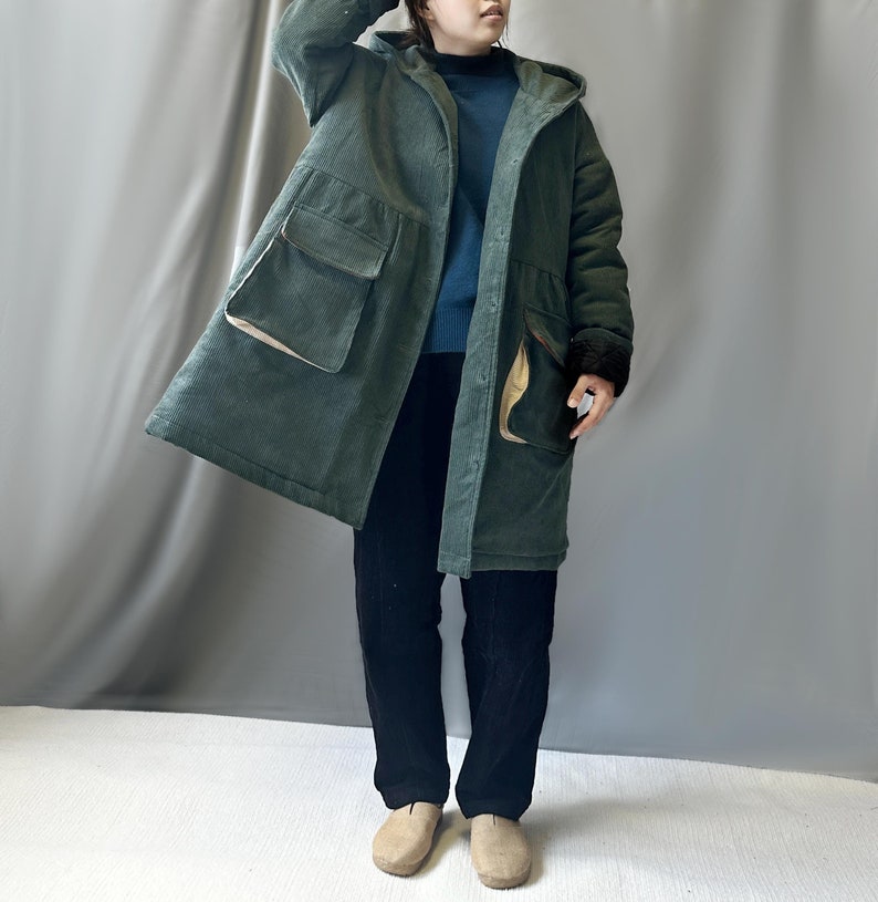 May include: A long, green corduroy coat with a hood and large pockets. The coat has a brown corduroy trim on the pockets and cuffs.
