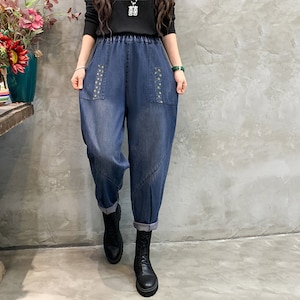 May include: Blue denim pants with a wide leg and a relaxed fit. The pants have a drawstring waistband and decorative stitching on the pockets.