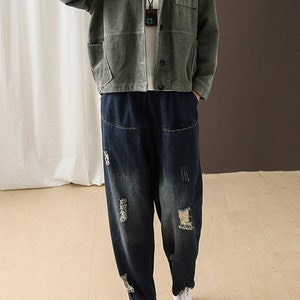 May include: A green corduroy jacket with a button-up front and a patch pocket on the left chest. The jacket is worn over a pair of dark blue distressed denim jeans with a loose fit.