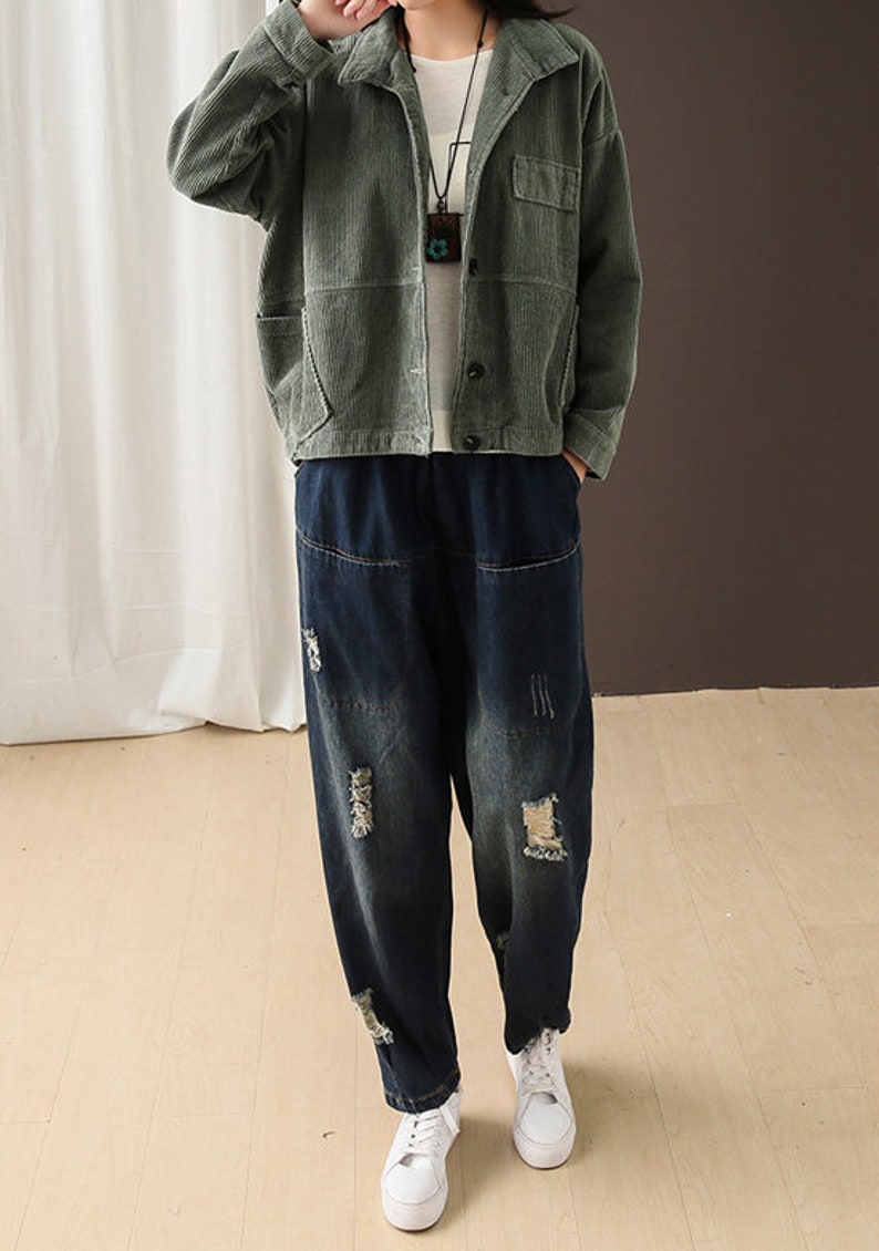 May include: A green corduroy jacket with a button-up front and a patch pocket on the left chest. The jacket is worn over a pair of dark blue distressed denim jeans with a loose fit.