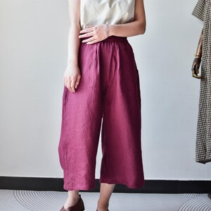 Puede incluir: Una camiseta sin mangas color crema combinada con pantalones anchos burdeos. Los pantalones tienen bolsillos grandes y un corte holgado. Zapatos de cuero marr&oacute;n completan el conjunto. La ropa es probablemente de lino o tejido transpirable similar.