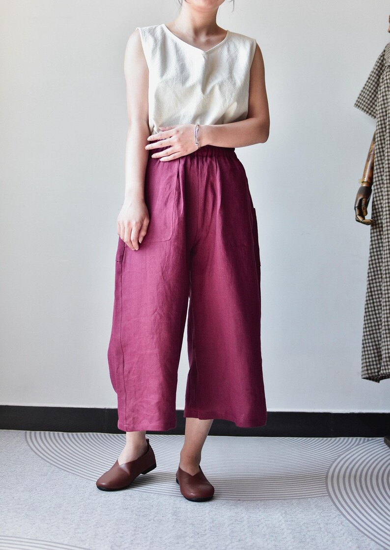 Puede incluir: Una camiseta sin mangas color crema combinada con pantalones anchos burdeos. Los pantalones tienen bolsillos grandes y un corte holgado. Zapatos de cuero marr&oacute;n completan el conjunto. La ropa es probablemente de lino o tejido transpirable similar.
