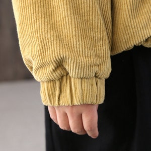 May include: A close-up of the cuff of a mustard yellow corduroy jacket. The fabric is soft and textured.
