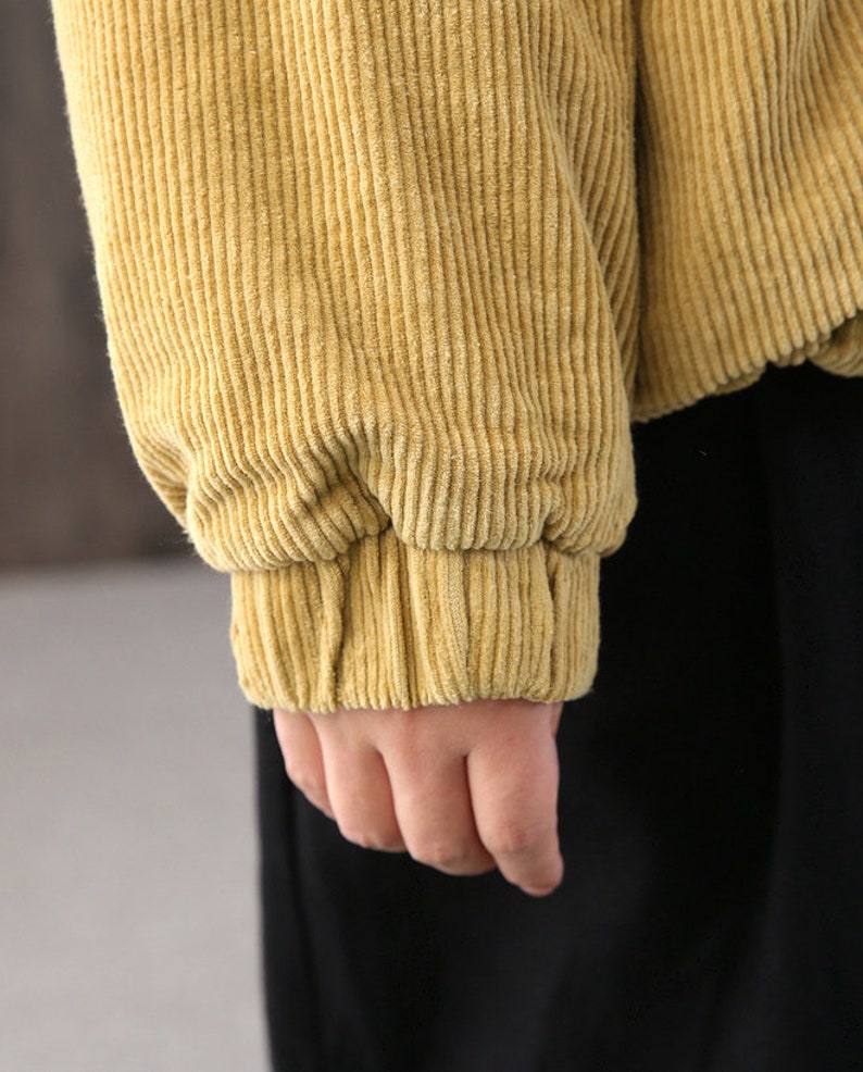 May include: A close-up of the cuff of a mustard yellow corduroy jacket. The fabric is soft and textured.
