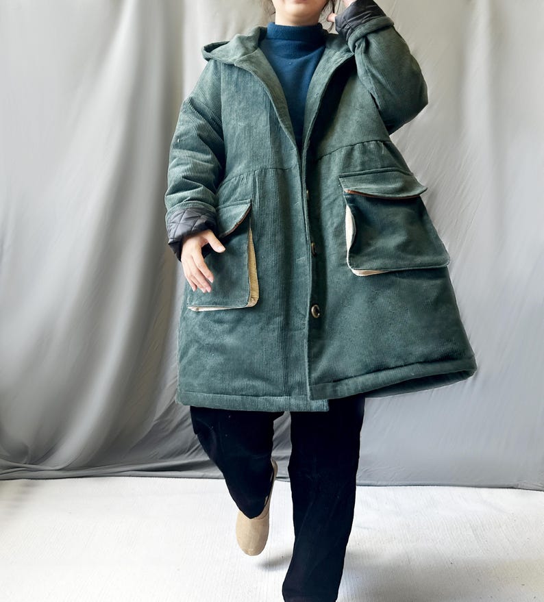 May include: A long, green corduroy coat with a hood and large pockets. The coat has a button closure and a relaxed fit.