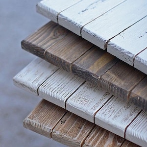 Può includere: Pila di quattro assi di legno, ciascuna dipinta di bianco con una finitura usurata. Le assi sono disposte a gradini, creando un aspetto rustico e stratificato.