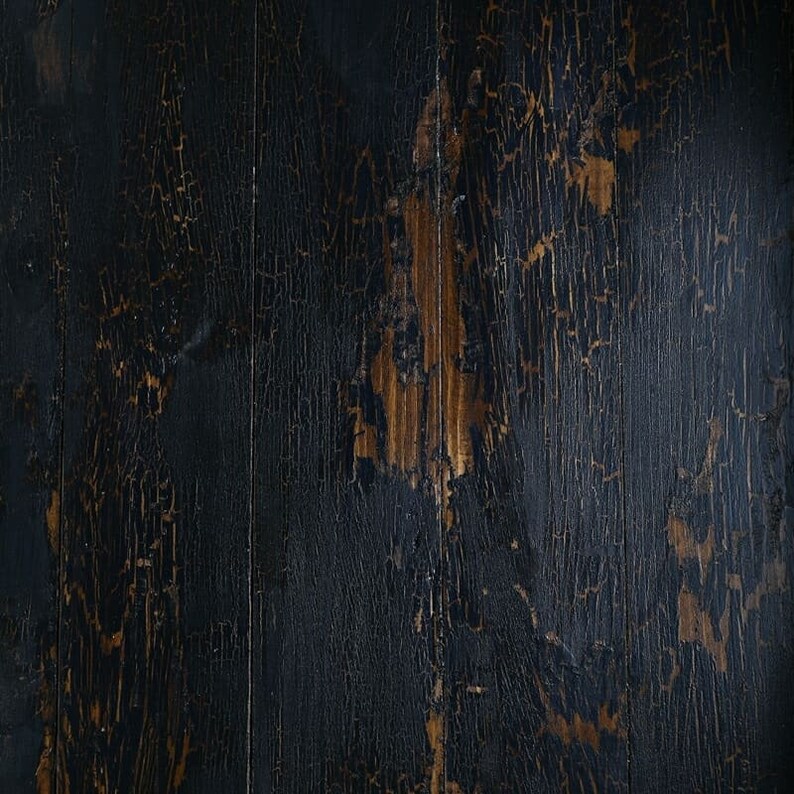 May include: Dark wood background with a distressed, cracked black paint finish. The wood grain is visible through the paint, creating a rustic and vintage look.