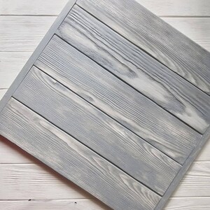 May include: A close-up of a gray wooden surface with a diagonal pattern. The wood has a weathered look and is painted a light gray color.