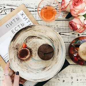 May include: A white ceramic plate with a brown and blue swirl design. The plate has a chocolate dessert and a small strawberry on it. The text "Пить есть жить" is visible on a brown paper background.