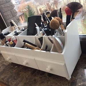 Peut inclure: Organisateur de maquillage en bois blanc avec trois tiroirs et plusieurs compartiments pour ranger les pinceaux de maquillage, les rouges &agrave; l&egrave;vres et autres cosm&eacute;tiques.