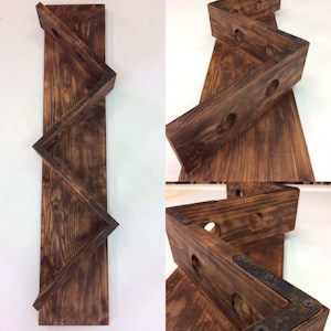 Puede incluir: Un estante de vino de madera con un diseño en chevron. El estante está hecho de madera marrón oscura y tiene detalles metálicos. Está diseñado para sostener botellas de vino.