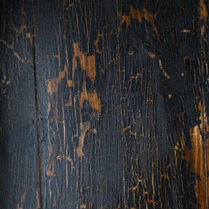May include: Close-up of a dark wood surface with a distressed, cracked finish. The wood has a natural grain pattern and shows signs of wear and tear, giving it a rustic and vintage look.