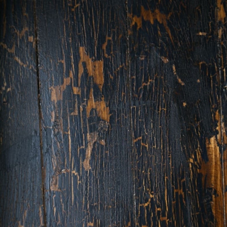 May include: Close-up of a dark wood surface with a distressed, cracked finish. The wood has a natural grain pattern and shows signs of wear and tear, giving it a rustic and vintage look.