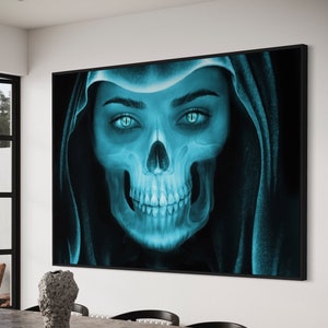May include: A digital art print of a woman's face with a skull overlay. The woman's eyes are blue and the skull is a light blue color. The print is framed in a black frame and hanging on a white wall.