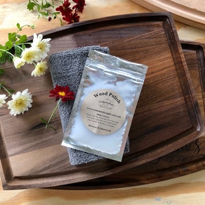 May include: A close-up of a wooden cutting board with a small bag of wood polish on top. The bag is labeled "Wood Polish" and has directions for use. The cutting board is made of walnut wood and has a natural finish. The bag of wood polish is a light brown color and has a white label with black text.