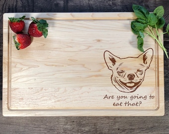 May include: A wooden cutting board with a brown chihuahua illustration and the text "Are you going to eat that?"  The board has a natural wood grain and is surrounded by strawberries and basil.