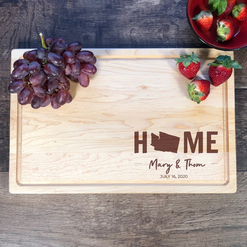 May include: A wooden chopping board with the words "HOME" and a silhouette of the state of Washington. The board is personalised with the names "Mary & Thom" and the date "JULY 16, 2020".