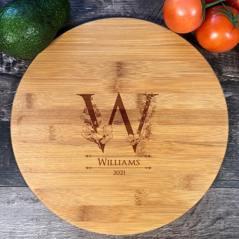 Puede incluir: Una tabla redonda de servir de bamb&uacute; con un dise&ntilde;o de monograma floral. El monograma es la letra "W" con un dise&ntilde;o floral a su alrededor. El texto "Williams 2021" est&aacute; grabado debajo del monograma.