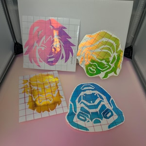 May include: Four colorful Cricut transfer stickers. The stickers feature designs of a lion's head, a robot, and an abstract design. The lion stickers are gold and pink. The robot sticker is blue and white. The abstract sticker is green and yellow.