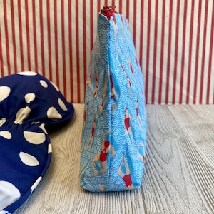 Peut inclure: Une trousse de maquillage bleue avec un motif de nageurs en maillots de bain rouges sur un fond ondul&eacute;. La trousse a une fermeture &eacute;clair rouge et est &agrave; c&ocirc;t&eacute; d'un article bleu et blanc &agrave; pois.