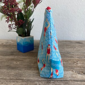 Peut inclure: Une trousse de maquillage bleu clair avec un motif de nageurs en maillots de bain rouges et bonnets blancs. Le sac a une fermeture &eacute;clair rouge et une petite &eacute;tiquette bleue avec le mot "ssen".