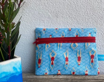 Peut inclure: Une pochette zippée bleue avec une fermeture éclair rouge et un motif de nageurs en maillots de bain rouges sur un motif de vagues bleu et blanc. La pochette a une étiquette blanche avec le texte "Kissis" dessus.