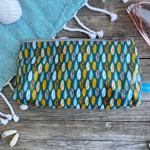 Peut inclure: Une pochette zippée turquoise avec un motif répétitif de plumes jaunes, blanches et brunes. La pochette est posée sur une surface en bois.