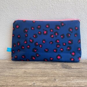 Könnte beinhalten: Eine blaue Reißverschlusstasche mit einem rosa Reißverschluss und einem Leopardenmuster. Die Tasche ist aus einem weichen, wasserabweisenden Material.