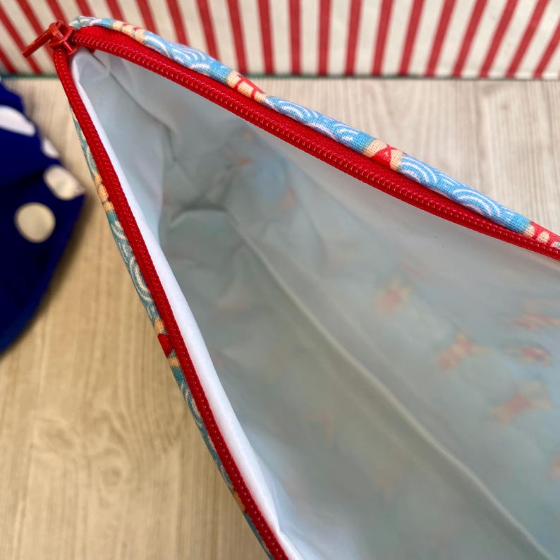 Peut inclure: Pochette ouverte avec une fermeture &eacute;clair rouge et un ext&eacute;rieur &agrave; motifs. L'ext&eacute;rieur de la pochette pr&eacute;sente un motif de vagues bleues et blanches avec des accents rouges. L'int&eacute;rieur est blanc. La fermeture &eacute;clair est rouge.