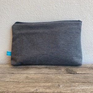 Pode incluir: Uma bolsa de zíper cinza com um zíper preto. A bolsa é feita de um tecido macio e texturizado.