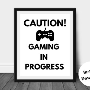 Pu&ograve; includere: Stampa con cornice nera con le parole "CAUTION! GAMING IN PROGRESS" e un'icona di controller. La stampa &egrave; su sfondo bianco. Un adesivo rotondo in basso a destra dice "Instant Download".
