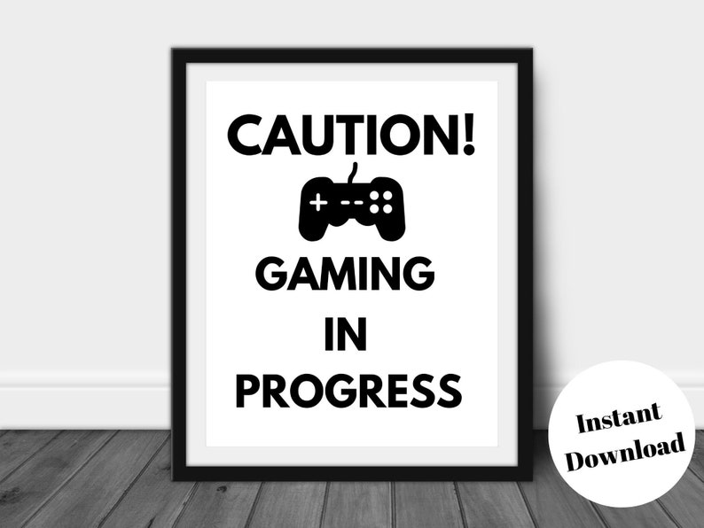 Pu&ograve; includere: Stampa con cornice nera con le parole "CAUTION! GAMING IN PROGRESS" e un'icona di controller. La stampa &egrave; su sfondo bianco. Un adesivo rotondo in basso a destra dice "Instant Download".