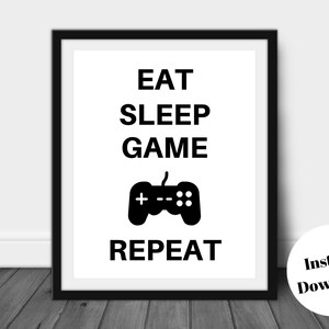 Pu&ograve; includere: Stampa con cornice nera con le parole "EAT SLEEP GAME REPEAT" in nero e un'icona di controller di gioco nera. Un cerchio bianco con "Instant Download" nell'angolo in basso a destra. Ideale per i giocatori.
