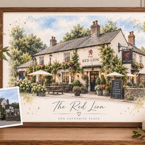 May include: A framed watercolor print of The Red Lion pub featuring a stone building with climbing greenery, outdoor seating, and a hanging sign. Below the illustration, the text reads The Red Lion, a heart icon, and OUR FAVOURITE PLACE.