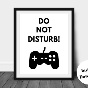 Pu&ograve; includere: Una stampa incorniciata con le parole "DO NOT DISTURB!" sopra una grafica nera di un controller di videogiochi. La stampa &egrave; in una cornice nera e ha uno sfondo bianco. Un adesivo circolare in basso a destra dice "Download istantaneo".