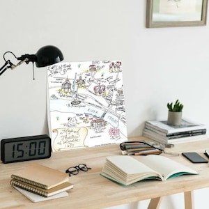 May include: A black desk lamp with a white desk and a hand-drawn map of London theaters from 1820. The map is framed and hanging on the wall. There are books, a digital clock, a tablet, and a phone on the desk.