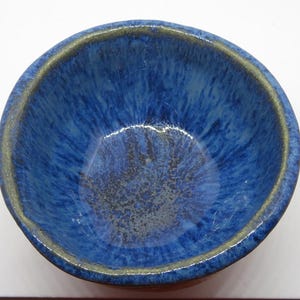 Op de afbeelding: Een blauwe keramische kom met een gespikkeld glazuur. De kom heeft een brede rand en een afgeronde bodem.