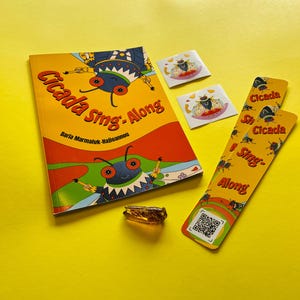 May include: A book titled Cicada Sing-Along by Daria Marmaluk-Hajioannou, two square stickers, two long bookmarks with QR codes, and a small amber-colored cicada figurine. The book cover features colorful illustrations of cicadas on a yellow background.