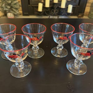 May include: Six clear glass stemmed drinking glasses with a red rim and a painted design of a red car. The glasses are arranged in two rows of three.