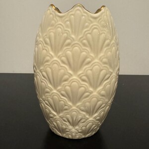 May include: A white ceramic vase with a gold rim and a textured design of overlapping fan shapes.
