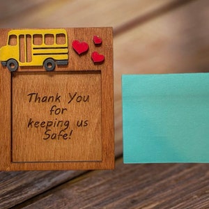 May include: Wooden frame featuring a yellow school bus and red heart decorations. The frame has the text "Thank You for keeping us Safe!" and a teal sticky note. The frame is made of wood.
