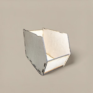 May include: A small, open-top wooden box with a geometric design. The box is constructed from light-coloured wood with a grey exterior. The edges are slightly uneven, and the box has a rectangular shape with angled sides.