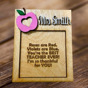Op de afbeelding: Houten fotolijst met een roze appeluitsparing en de tekst "Mrs. Smith". De lijst heeft een gegraveerd bericht dat luidt "Roses are Red. Violets are Blue. You're the BEST TEACHER EVER! I'm so thankful for YOU!"