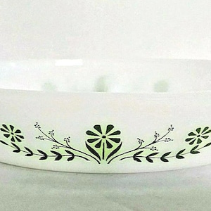 May include: White oval serving dish with a floral design in green and black. The dish has a simple, elegant shape with handles on either side. The floral pattern is a repeating design of stylized flowers and leaves.