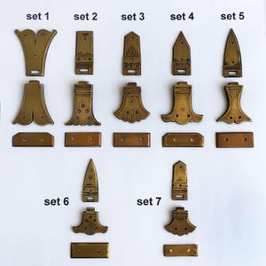 Könnte beinhalten: Sieben Sätze von Messingbeschlägen, angeordnet in Reihen und beschriftet von set 1 bis set 7. Jeder Satz enthält drei verschiedene Metallteile mit unterschiedlichen geometrischen und gravierten Mustern sowie vorgebohrten Löchern zur Befestigung.
